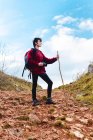 Tourist with backpack and stick looking away while hiking on hill road under cloudy sky in Spain — Stock Photo