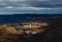 De arriba la fábrica en el valle contra la ciudad al pie de las montañas en el horizonte bajo el cielo gris nublado en Monsacro - foto de stock