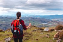 Back view of unrecognizable hiker with backpack and stick standing with arms outstretched and enjoying freedom viewing majestic scenery of countryside located along river shore in valley against foggy ridges at horizon under cloudy sky in Spain — Stock Photo