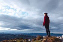 Турист стоя и наслаждаясь свободой просмотра величественные пейзажи сельской местности, расположенной вдоль берега реки в долине против туманных хребтов на горизонте под облачным небом в Испании — стоковое фото