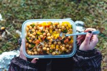 Von oben eine Frau in warmer Jacke mit einem Plastikbehälter mit Kichererbsen und Gemüse beim Mittagessen auf der Wiese beim Wandern in Spanien — Stockfoto