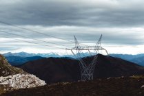 Grand pylône électrique avec câbles haute tension dans les hautes terres contre les crêtes de montagne enneigées à l'horizon sous un ciel gris nuageux en Espagne — Photo de stock