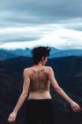 Rückenansicht einer oben ohne stehenden Frau mit erhobenen Armen, die Freiheit und Wildheit genießt, während sie die idyllische Landschaft eines nebligen Berges bei bewölktem Wetter in Spanien betrachtet — Stockfoto