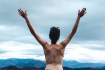 Обратный вид свободной топлесс женщины, стоящей с поднятыми руками, наслаждаясь свободой и дикостью при просмотре идиллических пейзажей туманной горы в пасмурную погоду в Испании — стоковое фото