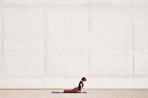 Vista lateral do atleta feminino na moda em sportswear fazendo exercício de ioga de cobra de bebê no tapete esportivo enquanto treina sozinho na rua — Fotografia de Stock