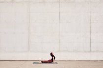 Vue latérale de la forme à la mode athlète féminine en vêtements de sport faire bébé cobra yoga exercice sur tapis de sport tout en s'entraînant seul dans la rue — Photo de stock