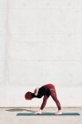 Vue latérale coupe tendance athlète féminine en vêtements de sport faisant large jambes courbées vers l'avant pose de yoga sur tapis de sport tout en s'entraînant seul — Photo de stock