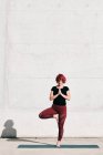 Selbstbewusste barfüßige Athletin in Sportbekleidung meditiert, während sie in Vrikshasana-Position steht, die Hände vor der Brust geschlossen — Stockfoto