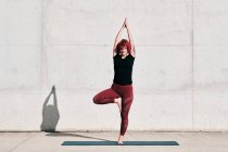 Впевнена босоніж жінка-спортсменка в спортивному одязі медитує, стоячи в положенні Врікшасана з піднятими руками і назвою — стокове фото
