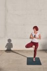 Selbstbewusste barfüßige Athletin in Sportbekleidung meditiert, während sie in Vrikshasana-Position steht, die Hände vor der Brust geschlossen — Stockfoto