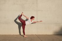 Trendy fitte Frau in Sportbekleidung macht Yoga in Herr der Tanz-Pose auf Sportmatte, während sie allein auf der Straße trainiert — Stockfoto