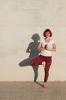 Fiduciosa atleta donna scalza in abbigliamento sportivo meditando mentre in piedi in posizione vrikshasana con le mani chiuse al petto in namaste — Foto stock