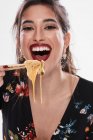 Trendy Frau mit stilvollem Make-up schaut in die Kamera mit Nudel im Mund und mit Essstäbchen isoliert auf weißem Hintergrund — Stockfoto