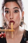 Trendy woman with stylish makeup looking at camera with noodle in mouth and using chopsticks isolated on white background — Stock Photo