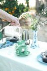 Woman pouring fresh milk from jug to ceramic mug while having picnic in garden — Stock Photo