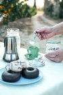 Mulher adicionando açúcar com colher de chá em copo de cerâmica verde de bebida saborosa enquanto prepara o café da manhã — Fotografia de Stock