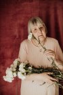 From above thoughtful old female with gray hair looking at camera and holding bouquet of white carnation at home — Stock Photo
