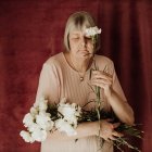 From above thoughtful old female with gray hair with closed eyes holding bouquet of white carnation at home — Stock Photo