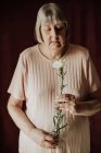 De haut réfléchie vieille femelle aux cheveux gris avec les yeux fermés tenant bouquet d'œillet blanc à la maison — Photo de stock
