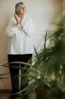 Pensionessa concentrata in camicetta bianca e pantaloni neri in piedi a parete facendo gesti con le mani e guardando altrove — Foto stock