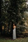 Стильна жінка спирається на стовбур дерева в лісі — стокове фото