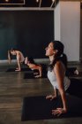 Вид сбоку босиком неузнаваемых женщин в спортивной одежде, концентрирующихся и делающих упражнения на спортивные коврики на деревянном полу против белых стен просторного зала — стоковое фото