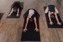 From above unrecognizable ladies in sportswear concentrating and lying in balasana position on sports mats on wooden floor in spacious workout room — Stock Photo