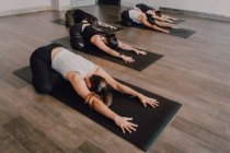 From above unrecognizable ladies in sportswear concentrating and lying in balasana position on sports mats on wooden floor in spacious workout room — Stock Photo