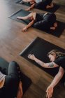 D'en haut dames méconnaissables en vêtements de sport se concentrant et couché en position balasana sur des tapis de sport sur le sol en bois dans une salle d'entraînement spacieuse — Photo de stock