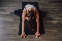 From above unrecognizable women in sportswear concentrating and lying in balasana position on sports mats on wooden floor in spacious workout room — Stock Photo