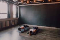 Зверху босоніж невпізнавані жінки в спортивному одязі концентрують і роблять дошку вправи на спортивних килимках на дерев'яній підлозі на білих стінах просторого залу — стокове фото