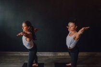 Le donne in abbigliamento sportivo fare guerriero pongono due esercizi di yoga in piedi su stuoie sportive nella moderna stanza di allenamento — Foto stock