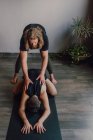 Жінка-інструктор у спортивному одязі навчає двох жінок, які лежать в позі баласани на спортивних килимках на дерев'яній підлозі у просторій тренувальній кімнаті — стокове фото