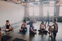 Angle élevé de jeunes femmes et hommes divers en vêtements de sport assis dans la pose du lotus et ayant des discussions d'intérêt tout en se reposant après une formation de groupe dans un studio de yoga contemporain — Photo de stock