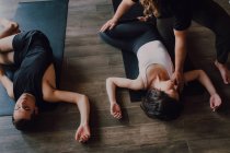 Alto ángulo de grupo de jóvenes deportistas y hombres en ropa deportiva con los ojos cerrados y las piernas cruzadas relajantes y respirando profundamente mientras yacen en posición savasana y meditando sobre alfombras deportivas en el moderno estudio de yoga - foto de stock
