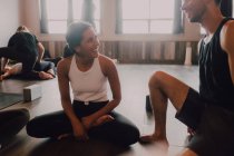 Высокий угол юных женщин и мужчин в спортивной одежде, сидящих в позе лотоса и интересующихся дискуссиями во время отдыха после групповых тренировок в современной студии йоги — стоковое фото