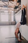 Vista lateral de cabeça para baixo do atleta feminino descalço em activewear praticando ioga em pose de cão voltado para baixo de pé e inclinado na parede branca do estúdio contemporâneo espaçoso — Fotografia de Stock
