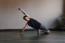 Atleta descalço diligente em sportswear praticando ioga no chão de madeira em espaçosa sala de treino contemporâneo — Fotografia de Stock