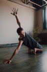 Диліжант босоніж спортсмен в спортивному одязі, що практикує йогу на дерев'яній підлозі в просторому сучасному тренувальному залі — стокове фото
