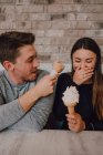 Hohe Winkel von gut gelaunten Mann und junge Frau in legerer Kleidung schauen einander mit leckerem Eis an, während sie am Tisch auf dem Sofa sitzen und es sich gemeinsam in einem modernen Café im Loft-Stil gemütlich machen — Stockfoto