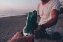 Друзья пьют пиво на пляже на закате — стоковое фото