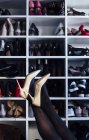 Crop female crossed legs in black tights and white high heel shoes with modern closet on background — Stock Photo