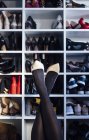 Crop female crossed legs in black tights and white high heel shoes with modern closet on background — Stock Photo