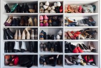 Modern white closet and square shelves with female colorful expensive high heels shoes and sneakers — Stock Photo