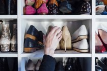 Cropped unrecognizable woman hands taking beige high heels shoes from shelf of modern white closet — Stock Photo