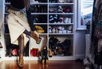 Crop femme anonyme dans une tenue élégante en essayant sur des bottes à talons hauts chaussures colorées dans une armoire moderne — Photo de stock