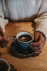 Dall'alto mani di raccolto di femmina irriconoscibile seduta a tavolo di legno che tiene il caffè caldo in una tazza rustica — Foto stock