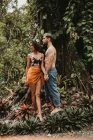 Loving sensual couple in light casual wear standing and holding hands among green tropical forest — Stock Photo