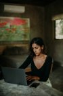 Серйозна зосереджена жінка друкує на ноутбуці, сидячи за столом на кухні сучасного мармуру стільниці — стокове фото