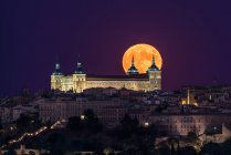 Wunderbare Kulisse eines beleuchteten antiken Palastes, der in bunter Nacht mit rotem Vollmond in Toledo über der Stadt erbaut wurde — Stockfoto